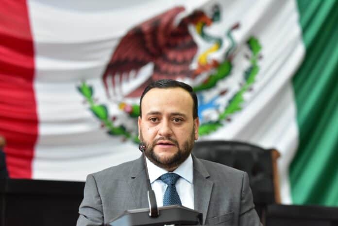 2356c453-cf3e-48ce-b0ea-719c39b47ebf Alta resolución de un hombre en traje durante una conferencia, con la bandera de México de fondo, representando temas de gobierno, política y liderazgo en Chihuahua.