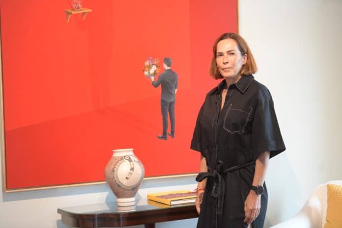 Elegante mujer en una galería de arte, vestida con un vestido negro, posando junto a una obra artística moderna en un ambiente cultural.