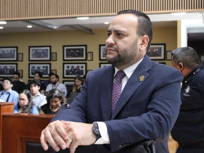 Rostro de un hombre en traje formal en una conferencia o reunión pública en Chihuahua, México, en un ambiente institucional y profesional.