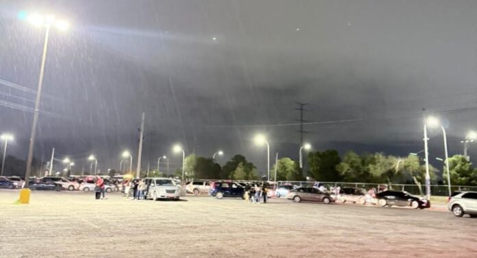 Nevado en la noche con lluvia, fila de autos y personas en estacionamiento, iluminación urbana y cielo nublado, aspecto de clima lluvioso en Chihuahua, ambiente húmedo y oscuro, imagen de clima adverso en la ciudad, aire húmedo y tormentoso en la noche.