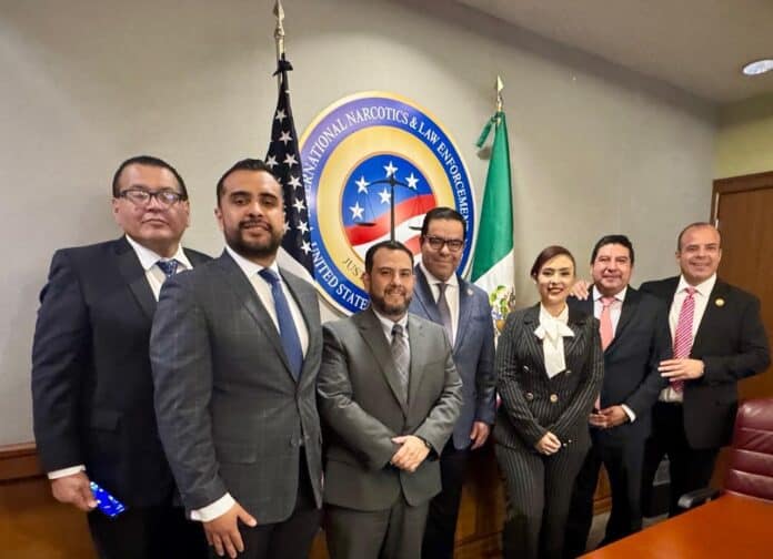 Agentes de law enforcement en una reunión oficial en una sala de conferencias con el emblema de Narcóticos y Ley, junto a banderas de Estados Unidos y México.