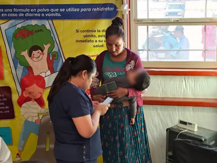 IMG-20250925-WA0016 Alto texto: Mujer con niño disfrutando en una clínica de salud en Chihuahua, México, con personal médico atendiendo y cartel informativo sobre salud infantil en español.