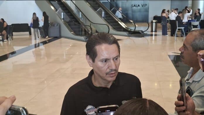 Screenshot_20250925_102437_Gallery Hombre siendo entrevistado en área de aeropuerto con fondo de escaleras y sala VIP, en un entorno contemporáneo y profesional.