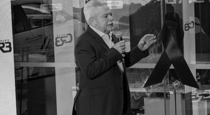 Hombre en evento de Soy Chihuahua, hablando frente a una presentación con lazo negro, simbolizando la lucha contra el cáncer de próstata, en un entorno profesional y comunitario.