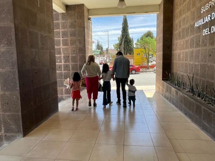 Familia caminando juntos en entrada de edificio en Chihuahua, México, en día soleado.
