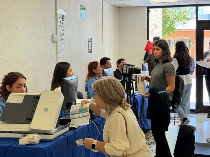 Tarjeta de identificación sanitaria en mano mujer en oficina de atención al cliente durante evento en exterior, atención personalizada, proceso de registro sanitario, servicios de salud en Chihuahua, atención ciudadana en oficina, trámites oficiales en Chihuahua, documento sanitario para servicios en Chihuahua, ayuntamiento, gobierno local, atención al usuario, proceso de gestión sanitaria, personal de atención al cliente en oficina, proceso de registro en Chihuahua, servicios públicos en Chihuahua, trámites en línea, evento oficial en Chihuahua, atención gubernamental, atención a la ciudadanía, gestión administrativa en Chihuahua, oficina de servicios, interacción ciudadana.
