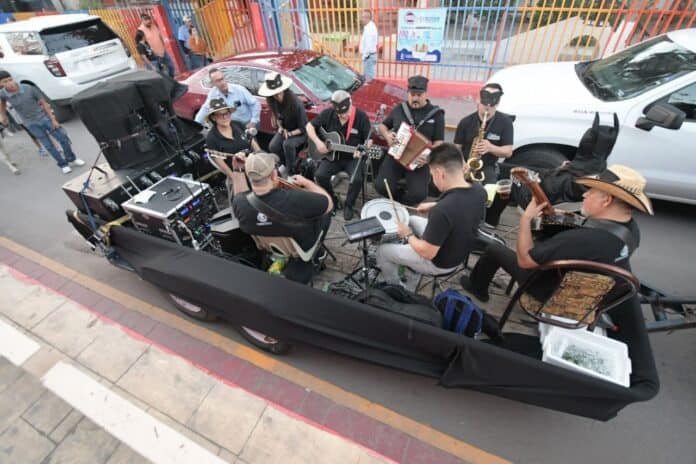 Ventanilla de música en vivo en las calles de Chihuahua con agrupación musical tocando instrumentos tradicionales y enmascarados, ambientando eventos culturales y festividades locales.