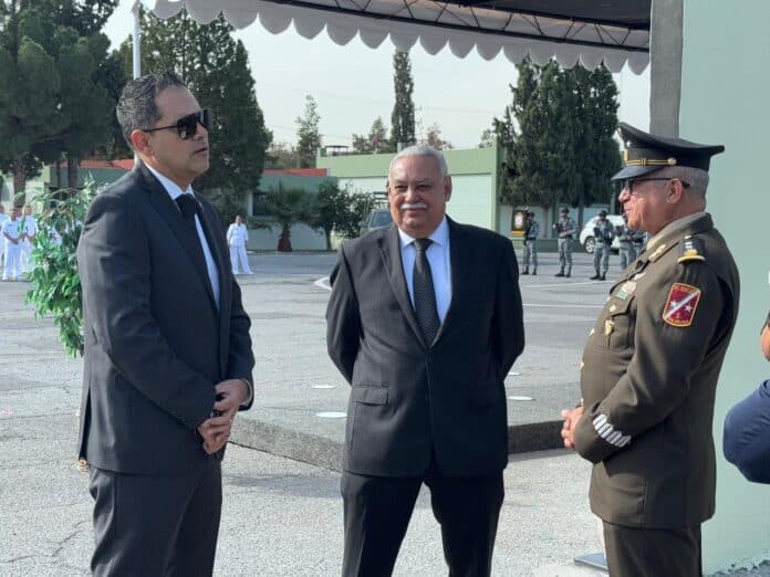 Funcionarios en ceremonia oficial en Chihuahua, México, con uniformes militares y civiles en un acto de protocolo, con autoridades y seguridad presente en un entorno formal y organizado, en un evento de alta importancia institucional.