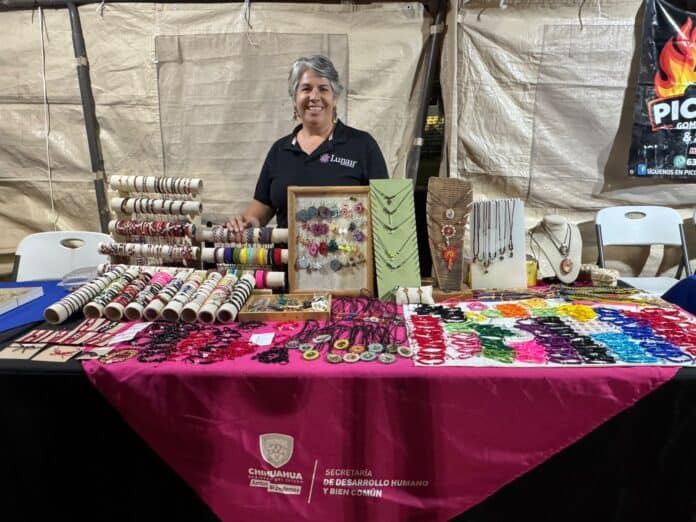 IMG-20251007-WA0013 Brochetas de pulseras y collares artesanales en un puesto de feria, con mujer sonriendo y exhibiendo accesorios de joyería hechos a mano en Chihuahua, México, promoviendo productos artesanales y cultura local.