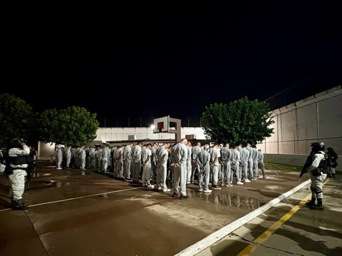 IMG-20251008-WA0005 Hombres en uniforme y armas, en una fila con las manos en la espalda, en una audiencia de reclusión en un campo de juego, en la noche, en Chihuahua, México.