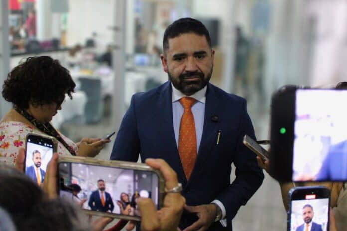 Representante o funcionario en entrevista durante evento en oficinas, rodeado de periodistas con smartphones en un entorno profesional en Chihuahua, México.