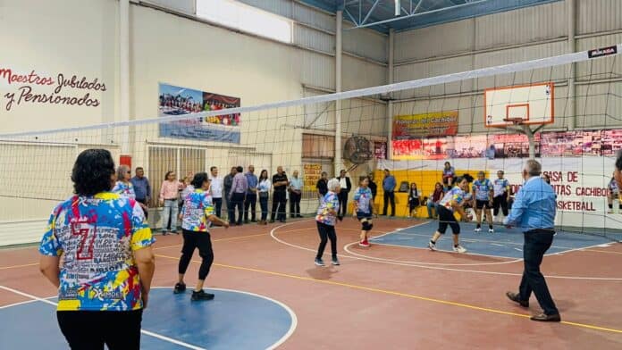 Jugadores de voleibol en acción en una cancha cubierta en la Casa de los Abuelos y Pensionados del Cachíbol, en Chihuahua, promoviendo deporte y recreación para adultos mayores.