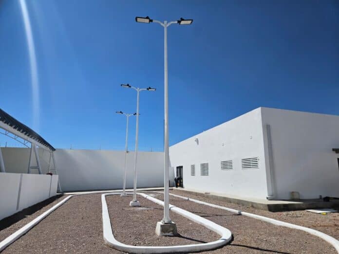 IMG-20251012-WA0001 Teléfonos públicos en exteriores bajo cielo azul con estructura metálica y piso de gravilla, en un entorno moderno y minimalista con paredes blancas.