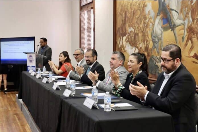 Empresarios y funcionarios en rueda de prensa sobre políticas públicas y desarrollo en Chihuahua, en un evento formal con reconocimiento, en un entorno profesional y artístico.