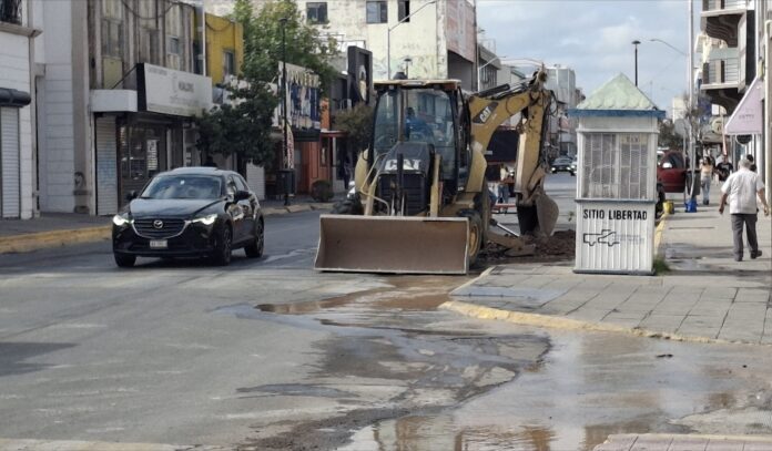 Camioneta y maquinaria en reparación vial en la calle, con presencia de vehículos y peatones en zona urbana de Chihuahua, para mantenimiento de calles y servicios urbanos.