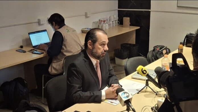Screenshot_20251009_115715_Gallery Panorámica de entrevista de prensa con hombre en traje sentado en mesa con micrófonos y cámaras en estudio de noticias cobertura de medios en medios de comunicación en chihuahua México.