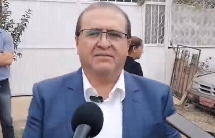 Nene con gafas y traje azul durante entrevista en exterior, fondo con personas y autos en Chihuahua.